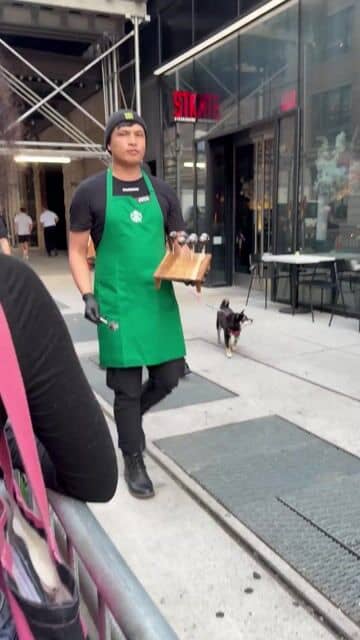 A Roastery barista in a green apron carrying a wooden tray of chocolate cake pops down the line on 15th Street