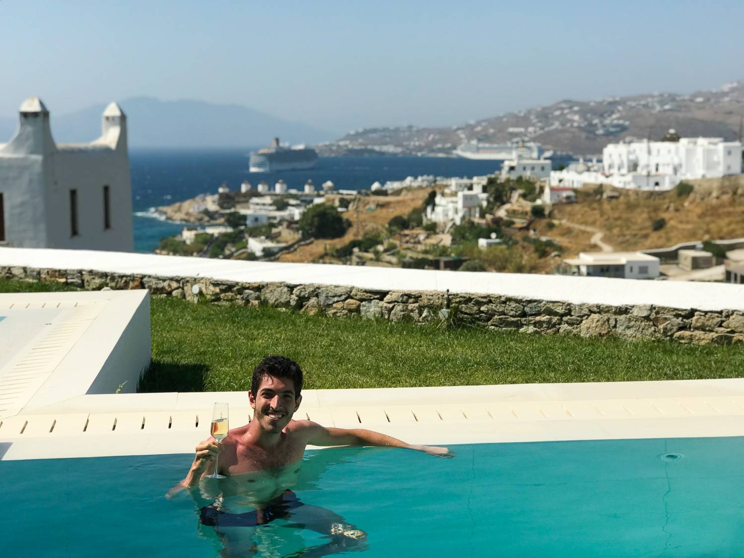 Rocky in a pool overlooking Mykonos, whitewashed buildings, and the Aegean Sea.