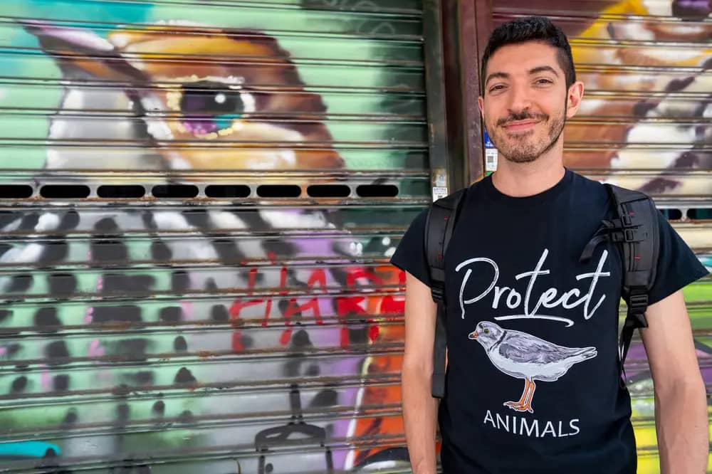 Rocky Trifari beside a colorful bird mural, wearing a Protect Animals shirt