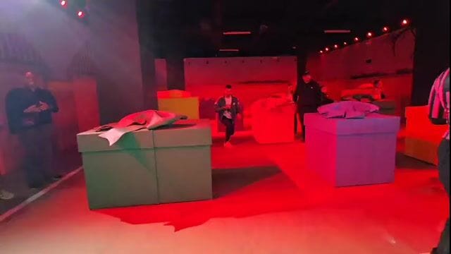 Inside the Red Light, Green Light room: guards walking between oversized gift boxes under red light
