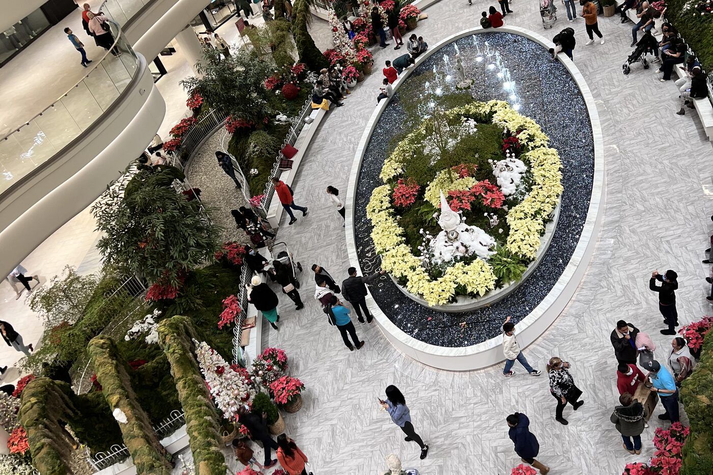 An overhead view of a mall atrium with a large circular flower display and holiday decoration