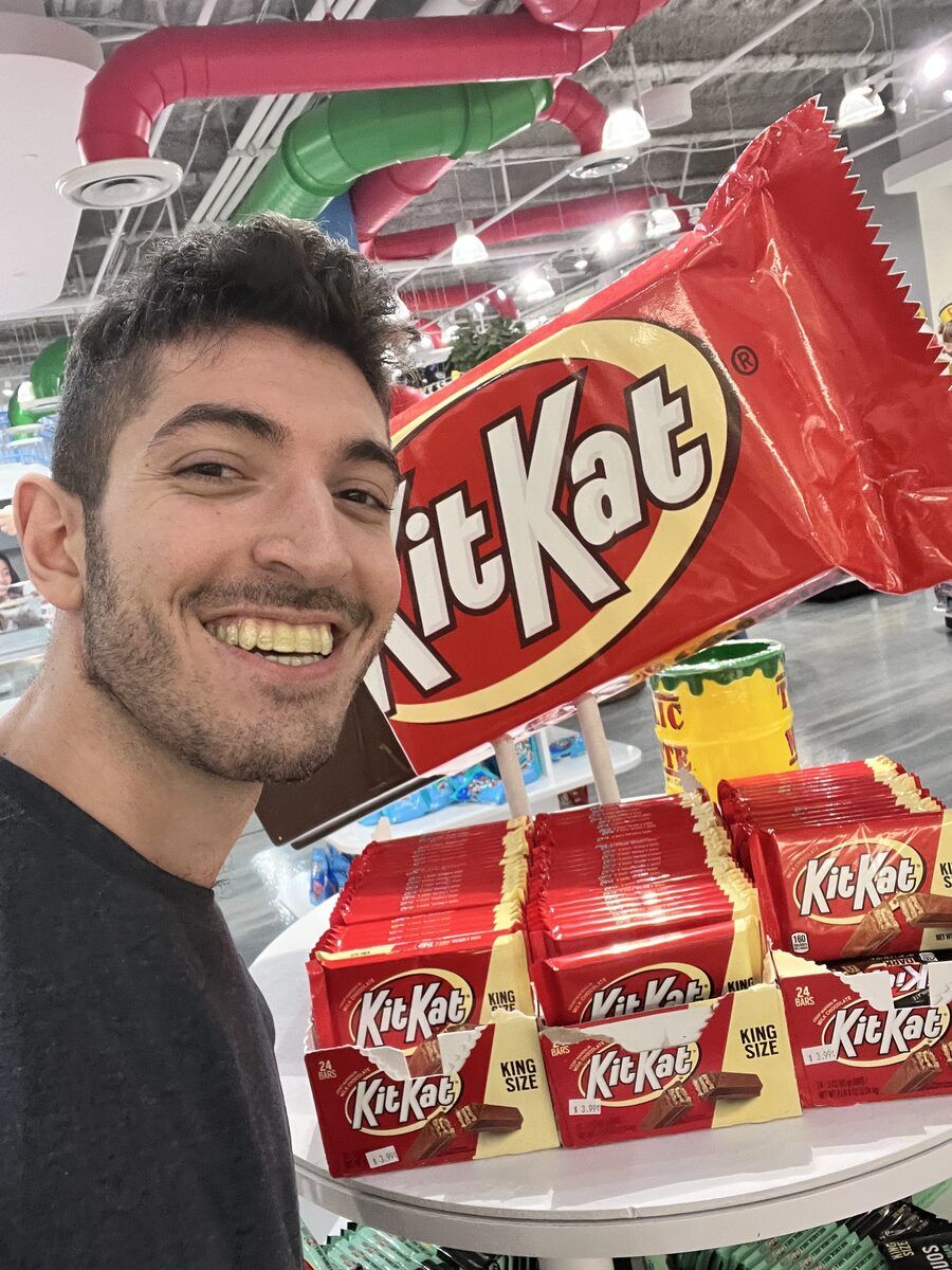 Rocky smiling next to an oversized Kit Kat display in a sweet shop