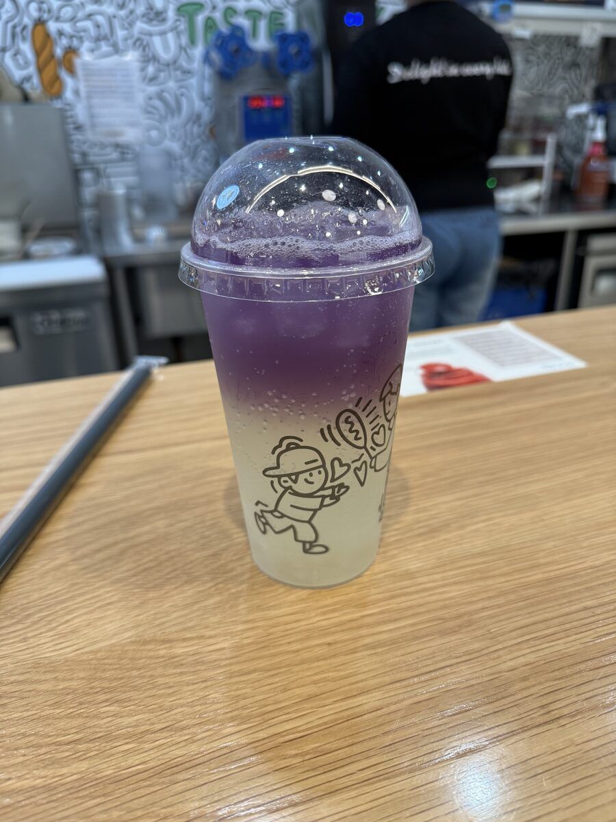 A tall cup of purple and clear layered lemonade on a wooden table