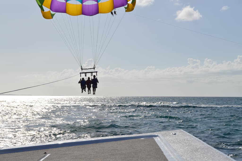 A parasail canopy carrying three people high above the sea