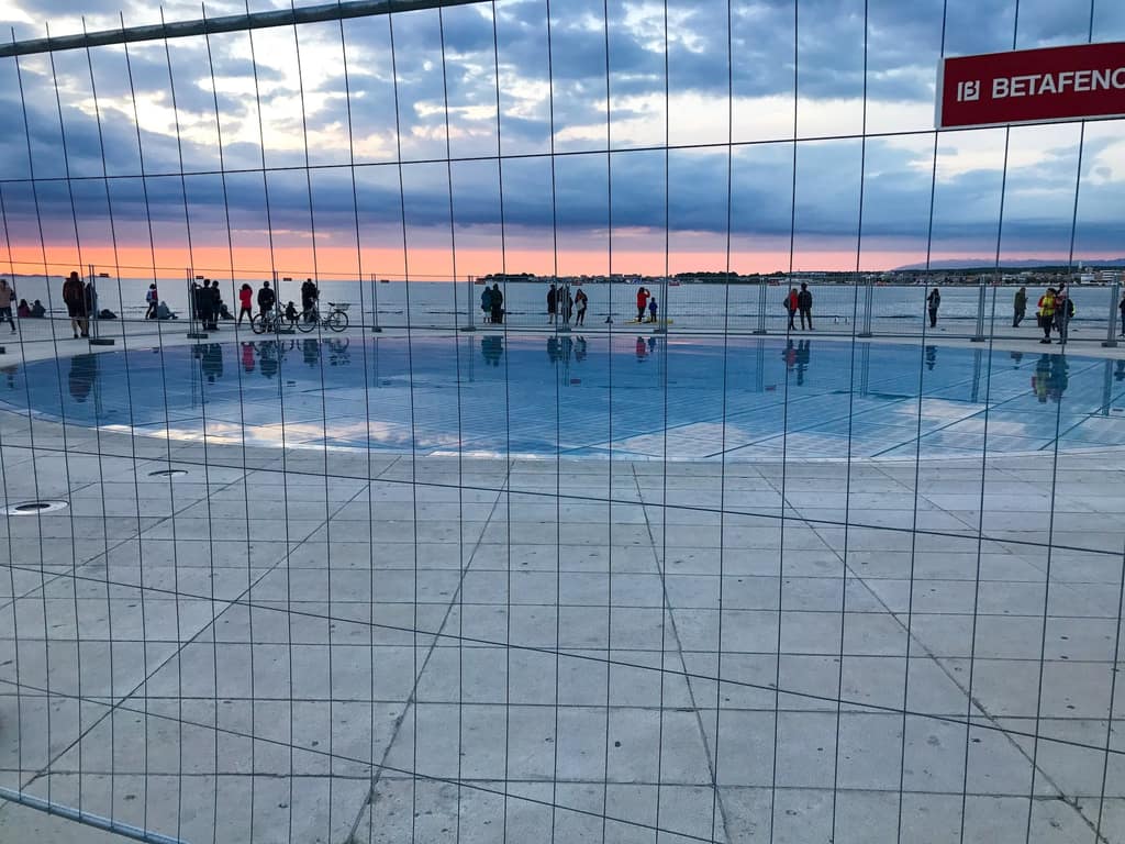 The Greeting to the Sun behind a chain-link construction fence