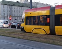 A yellow Warsaw tram on a city street at dusk