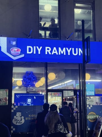 A bright blue DIY Ramyun sign over the entrance at Speedy Korea Grill, with a neon polar bear in the window