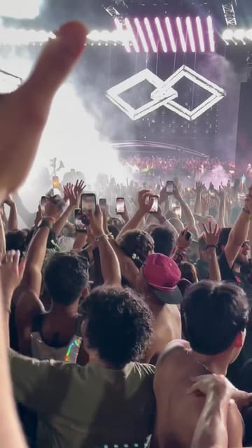 Hands and phones up in a packed crowd in front of the main stage, the Experts Only double-diamond logo glowing over the smoke