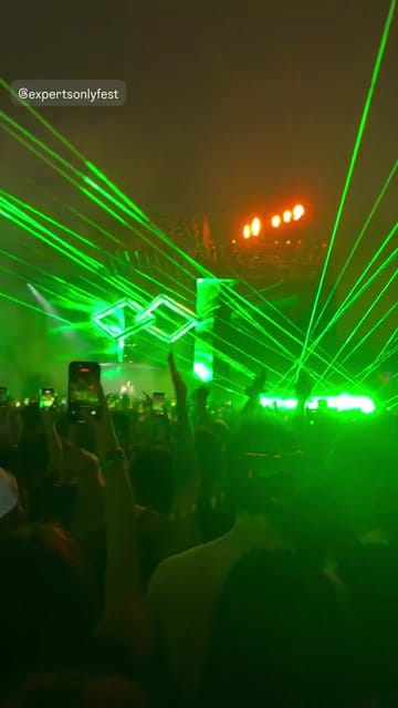 Green lasers slicing through the dark over a crowd holding up phones, the stage glowing green