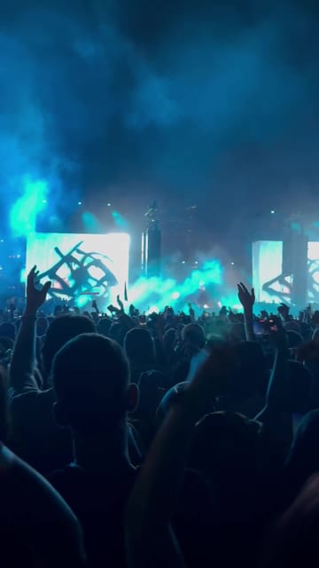 The main stage bathed in cyan light and smoke, the screens showing the Experts Only logo, hands in the air