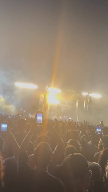 Golden stage lights flaring through thick smoke over a crowd holding up phones