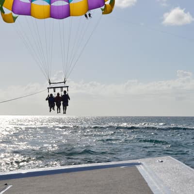 A parasail canopy carrying three people high above the sea