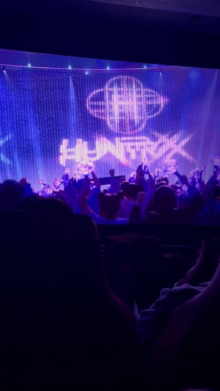 The opening concert of KPop Demon Hunters on the big screen at Regal Times Square, a stage lit purple over the silhouettes of the audience