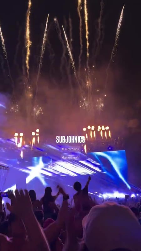 Gold fireworks shooting up over the main stage during SUBJOHNICS, flames along the stage roof and blue light on the screens