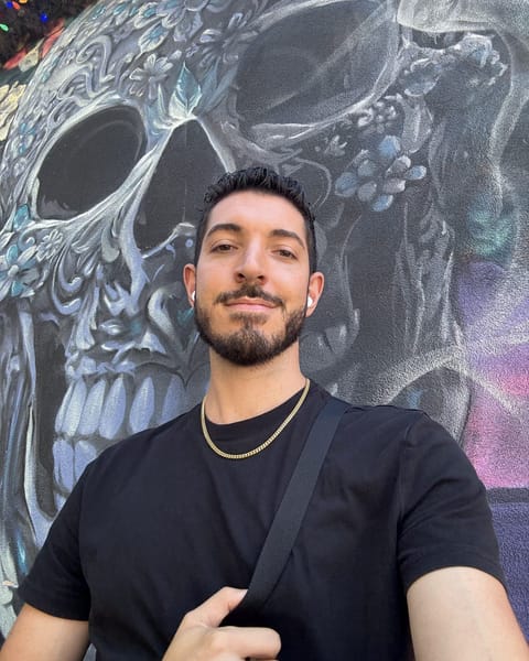 Rocky taking a selfie in front of a huge painted skull mural in Hell's Kitchen, wearing a black tee and a gold chain