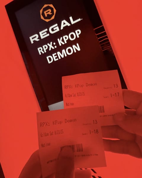Two Regal ticket stubs for RPX KPop Demon Hunters, 6:10pm Saturday 8/23/25, theatre 13, seats I-17 and I-18, held up in front of a lit Regal RPX sign