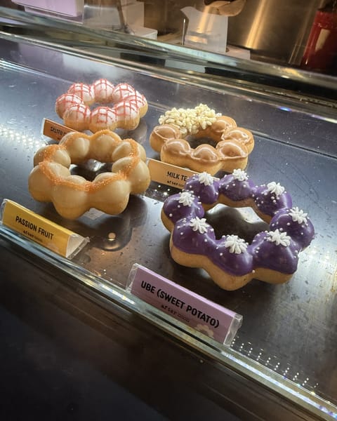 Mochi donuts in a glass case at Mochi Mochi Donut, including passion fruit, milk tea and a purple ube donut with white piped flowers