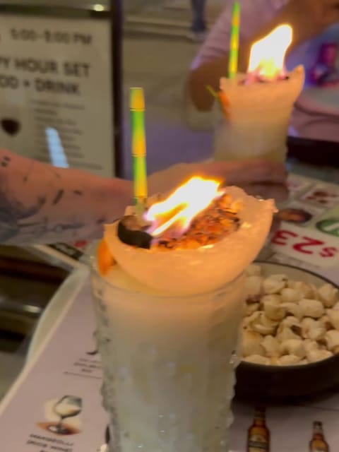 A tall white coconut cocktail in a hobnail glass at UT47 with flames leaping from its toasted coconut topping