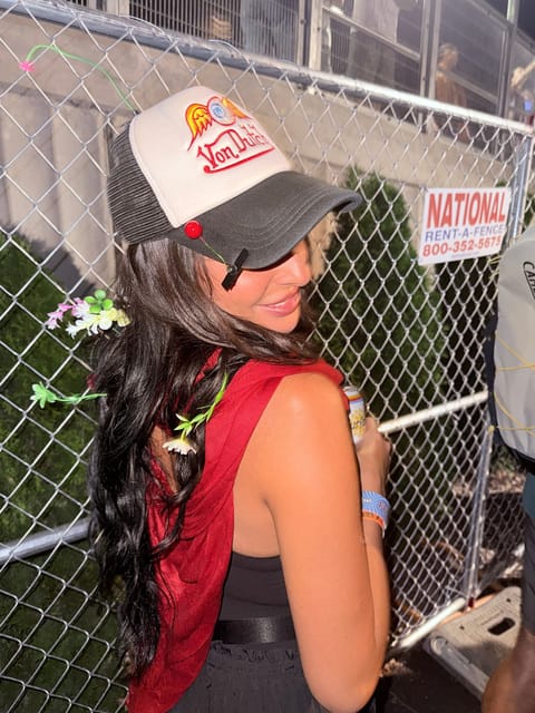 Tiffany smiling over her shoulder by a chain-link fence, sprout clips tucked all through her hair and on her hat