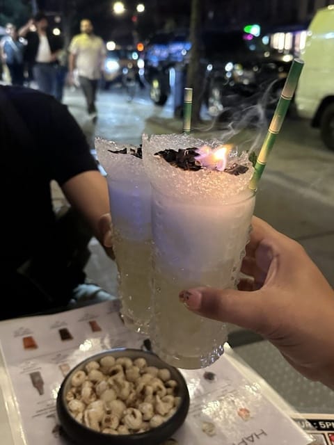 Two flaming Coco number 47 cocktails clinking together over a table on 9th Avenue at night