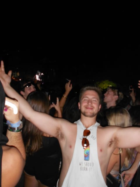 Zach dancing with both arms out wide and a big smile in the crowd at night