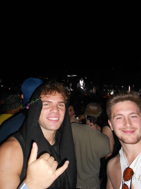 Nick with a sprout clip on his head throwing a shaka next to Zach in the crowd at night