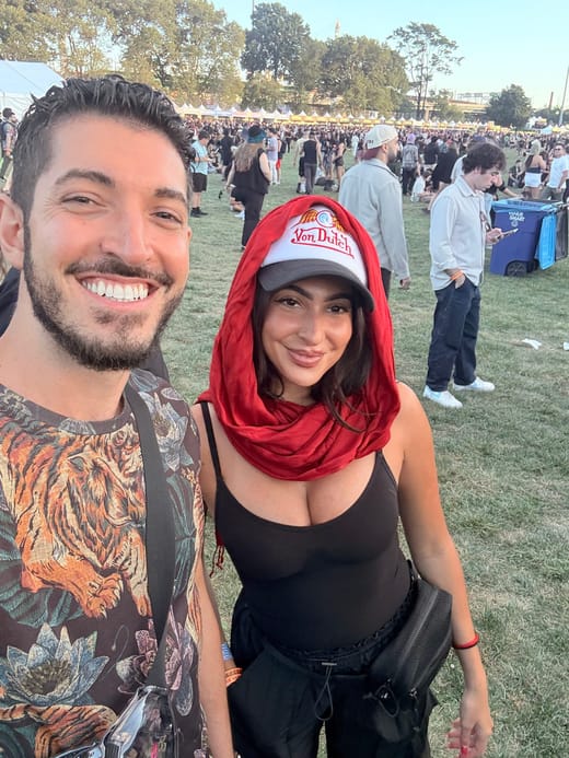 Rocky and Tiffany taking a selfie on the festival lawn in early evening sun, crowds and white tents behind them