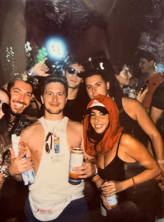 An instant photo of the group at night: Rocky, Zach, Nick, Vinny and Tiffany squeezed together and smiling, with more festival-goers behind