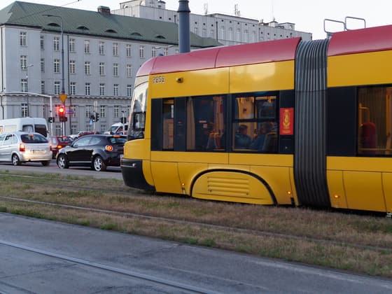 A yellow Warsaw tram on a city street at dusk