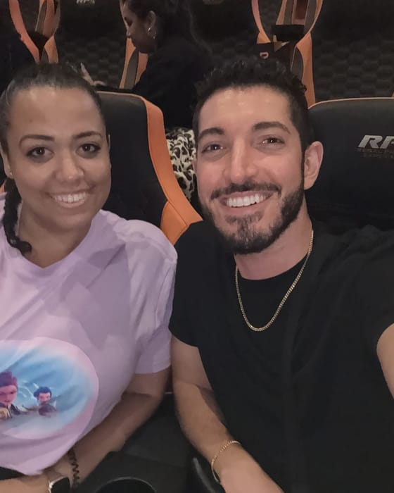 Rocky and his friend Carolyn smiling in orange-and-black recliner seats in the RPX auditorium at Regal Times Square, Carolyn in a lavender KPop Demon Hunters tee