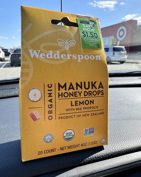 A box of Wedderspoon Organic Manuka Honey Drops, lemon with bee propolis, 20 count, on a car dashboard