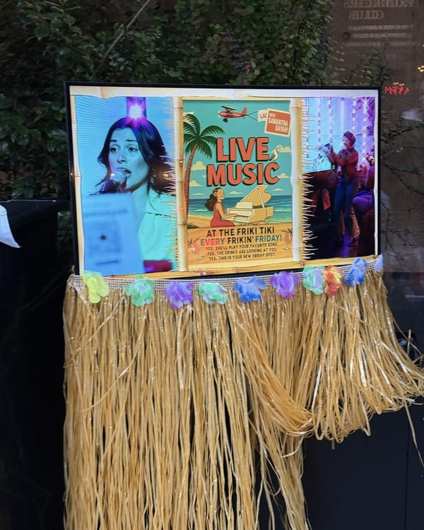 A sign on a grass skirt outside The Friki Tiki advertising live music with Samantha Sayah, with a cartoon of a woman at a piano on a beach