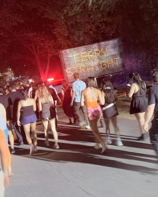Festival-goers walking out at night past an LED road sign reading Ferry Straight
