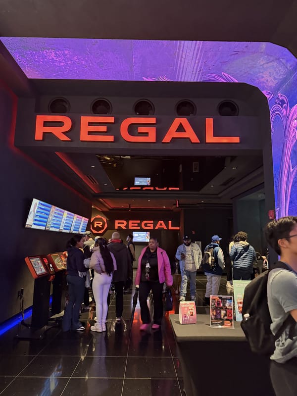 The red REGAL sign over the entrance to Regal Times Square on West 42nd Street, with people in the lobby