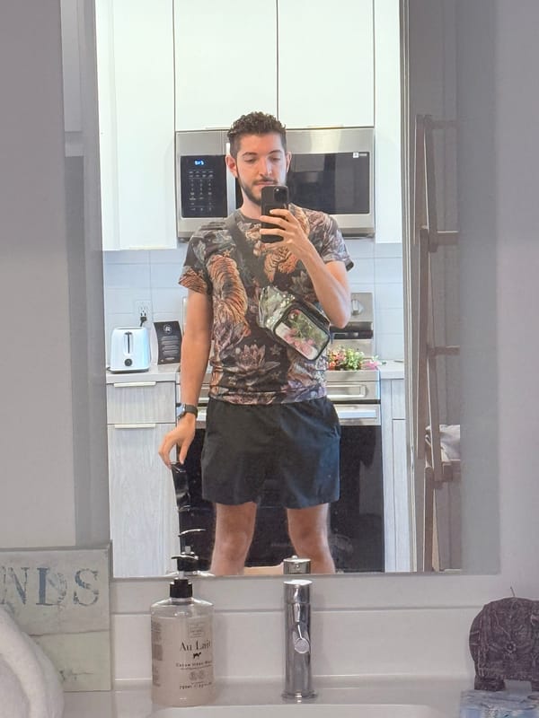 Rocky taking a mirror selfie at home in a tiger-print T-shirt and black shorts, a clear crossbody bag across his chest