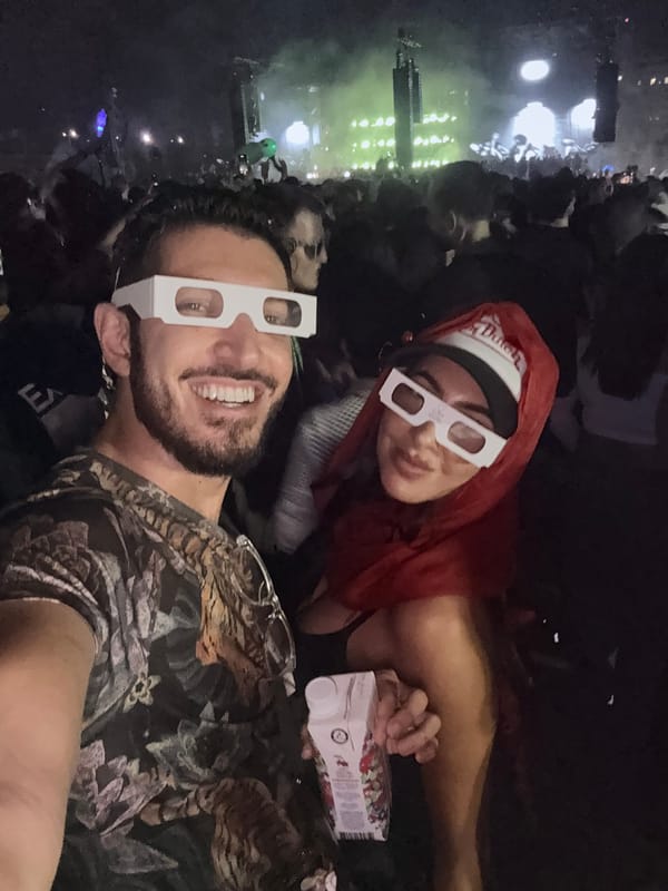 Rocky and Tiffany grinning in white cardboard glasses in the dark crowd, green stage lights behind them