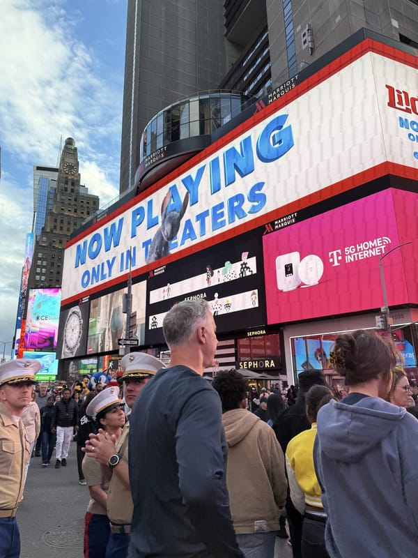 US Marines in dress uniforms and white covers in Times Square during Fleet Week, under a Lilo and Stitch Now Playing Only in Theaters billboard