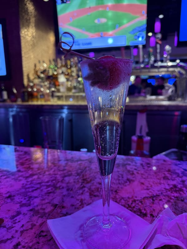 A pink cocktail and a beer on a marble bar under purple light