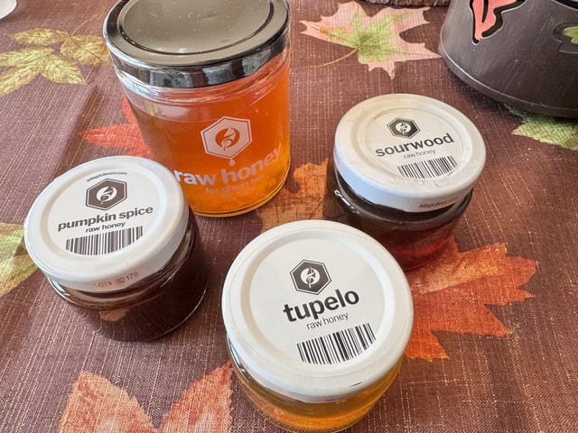 Adagio honey jar lids labelled pumpkin spice, sourwood and tupelo next to a big raw honey jar
