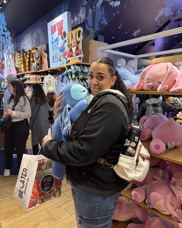 Carolyn hugging a giant blue Stitch plush inside Miniso, with shelves of pink Angel plushies behind her