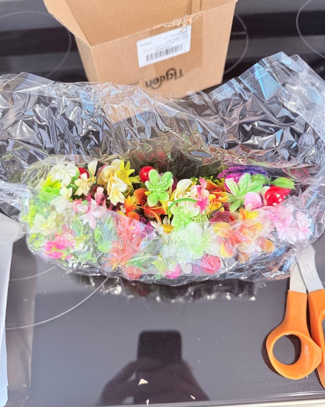 A clear bag stuffed with dozens of tiny artificial flower and sprout hair clips in pink, yellow, white and green, fresh out of a cardboard box