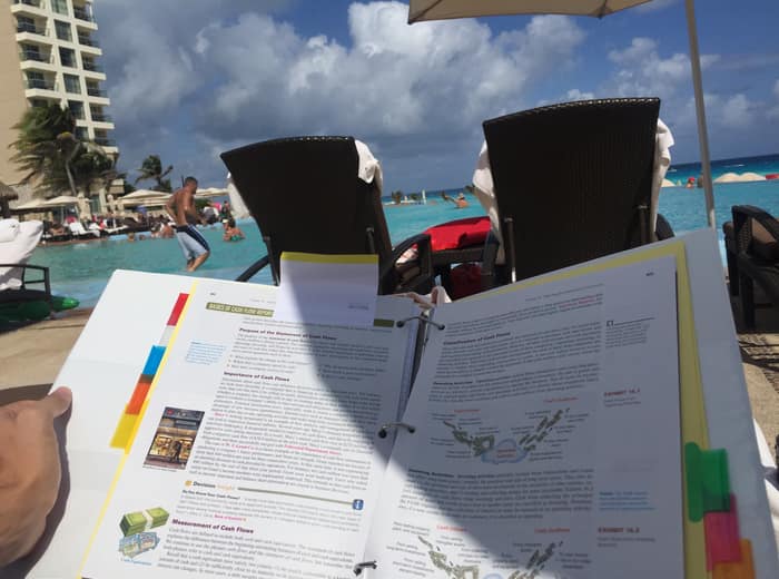 A printed assignment and a laptop on a beach lounger with the resort behind