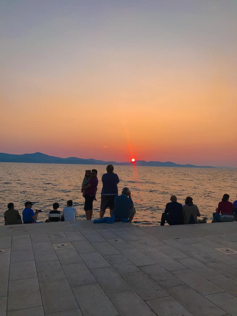 People sitting on the Sea Organ steps silhouetted against the sunset